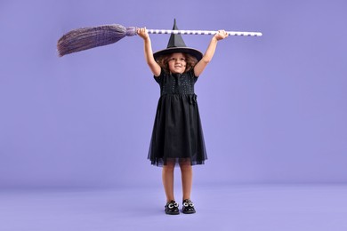 Photo of Funny girl with broom dressed like witch for Halloween celebration on violet background