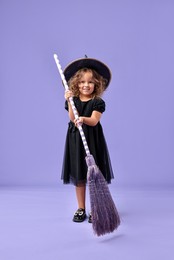 Photo of Funny girl with broom dressed like witch for Halloween celebration on violet background