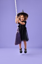 Photo of Funny girl with broom dressed like witch for Halloween celebration on violet background