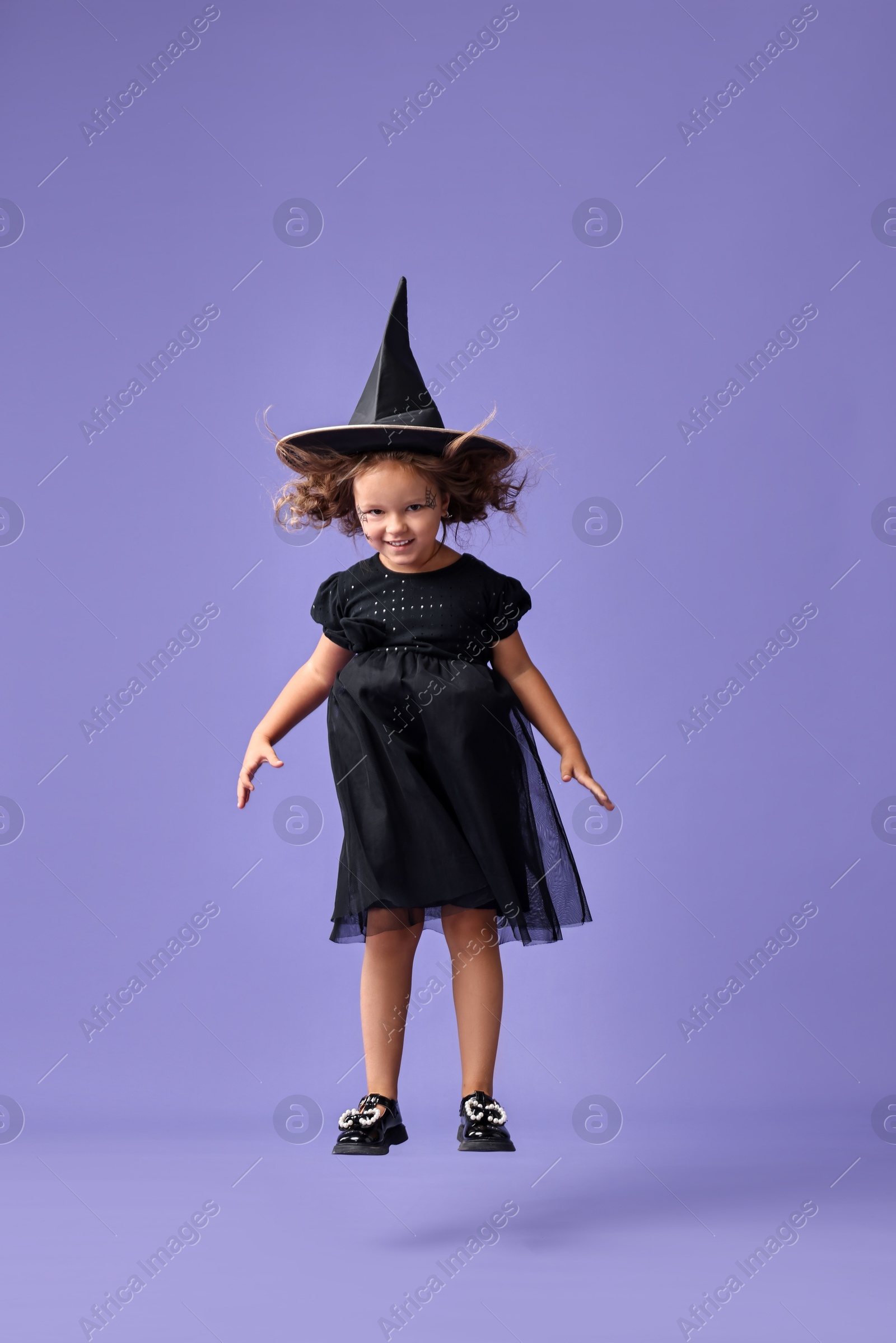 Photo of Funny girl dressed like witch on violet background. Halloween celebration