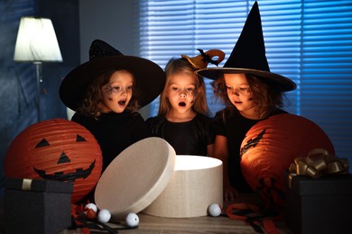 Surprised girls in costumes with festive decor and gift boxes indoors at night. Halloween celebration