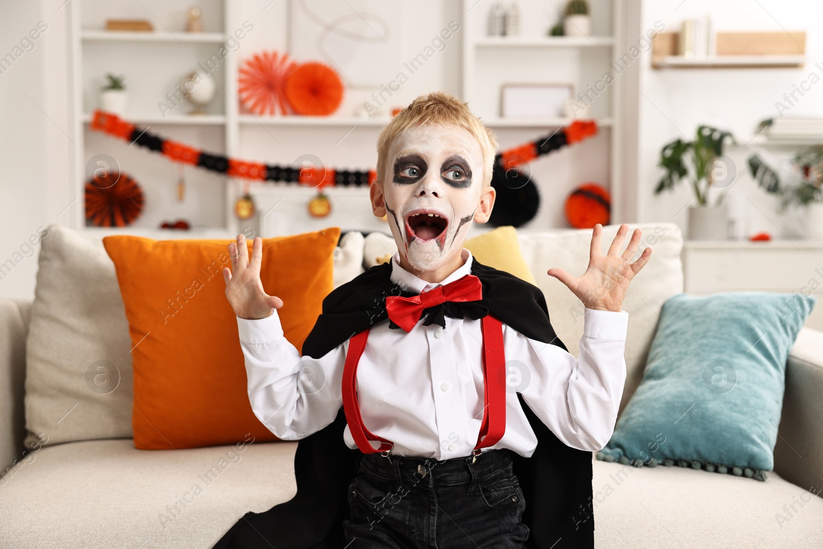 Photo of Funny boy dressed like vampire for Halloween celebration on sofa in room