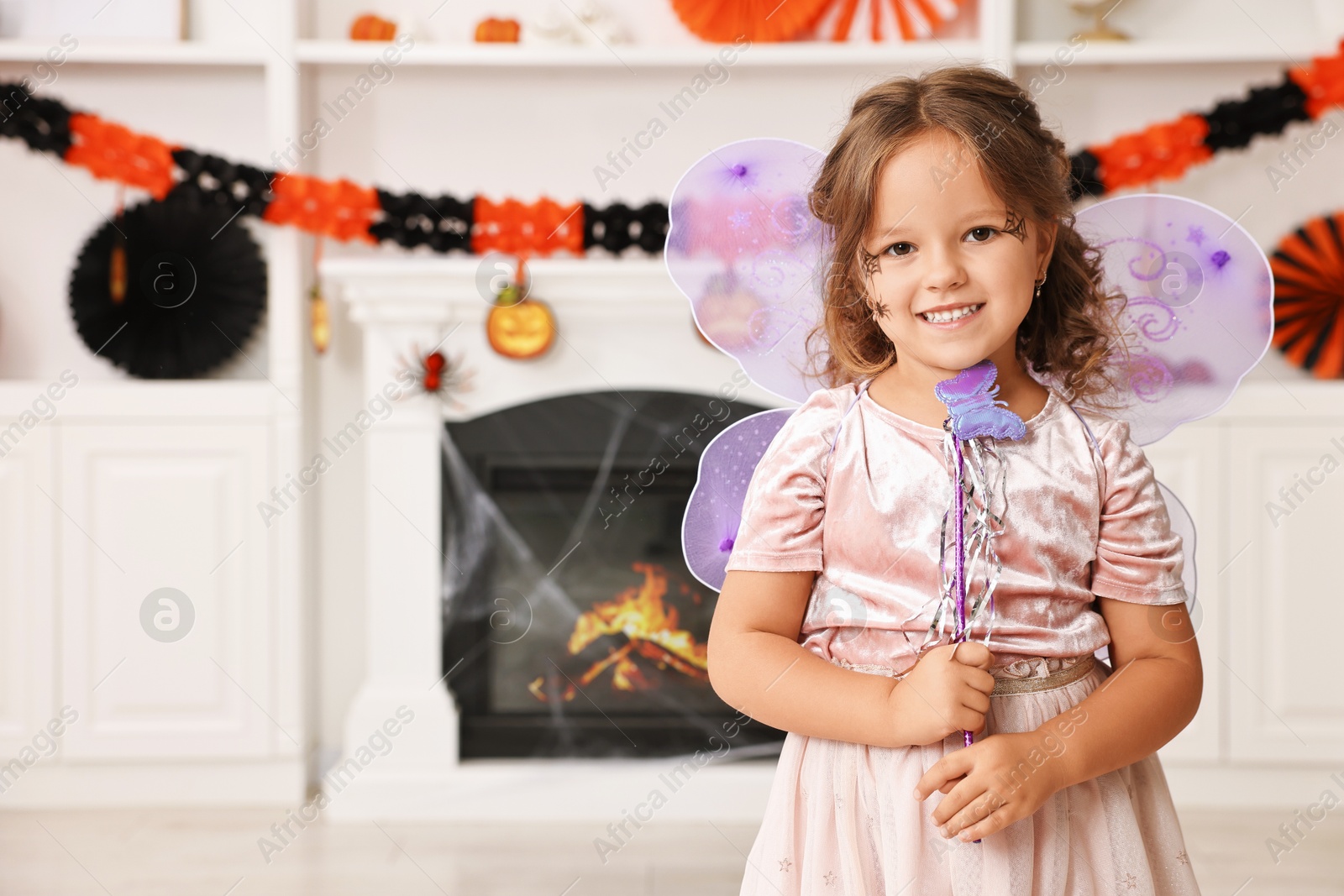 Photo of Cute girl dressed like fairy with magic wand in room, space for text. Halloween costume