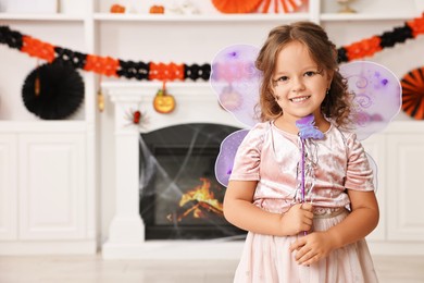 Photo of Cute girl dressed like fairy with magic wand in room, space for text. Halloween costume