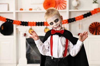 Photo of Funny boy dressed like vampire for Halloween celebration in room