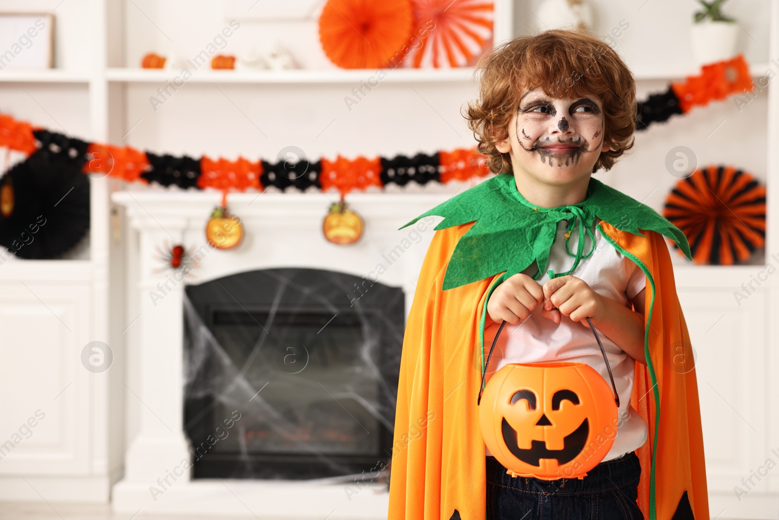 Photo of Funny boy with bucket dressed like pumpkin in room, space for text. Halloween celebration