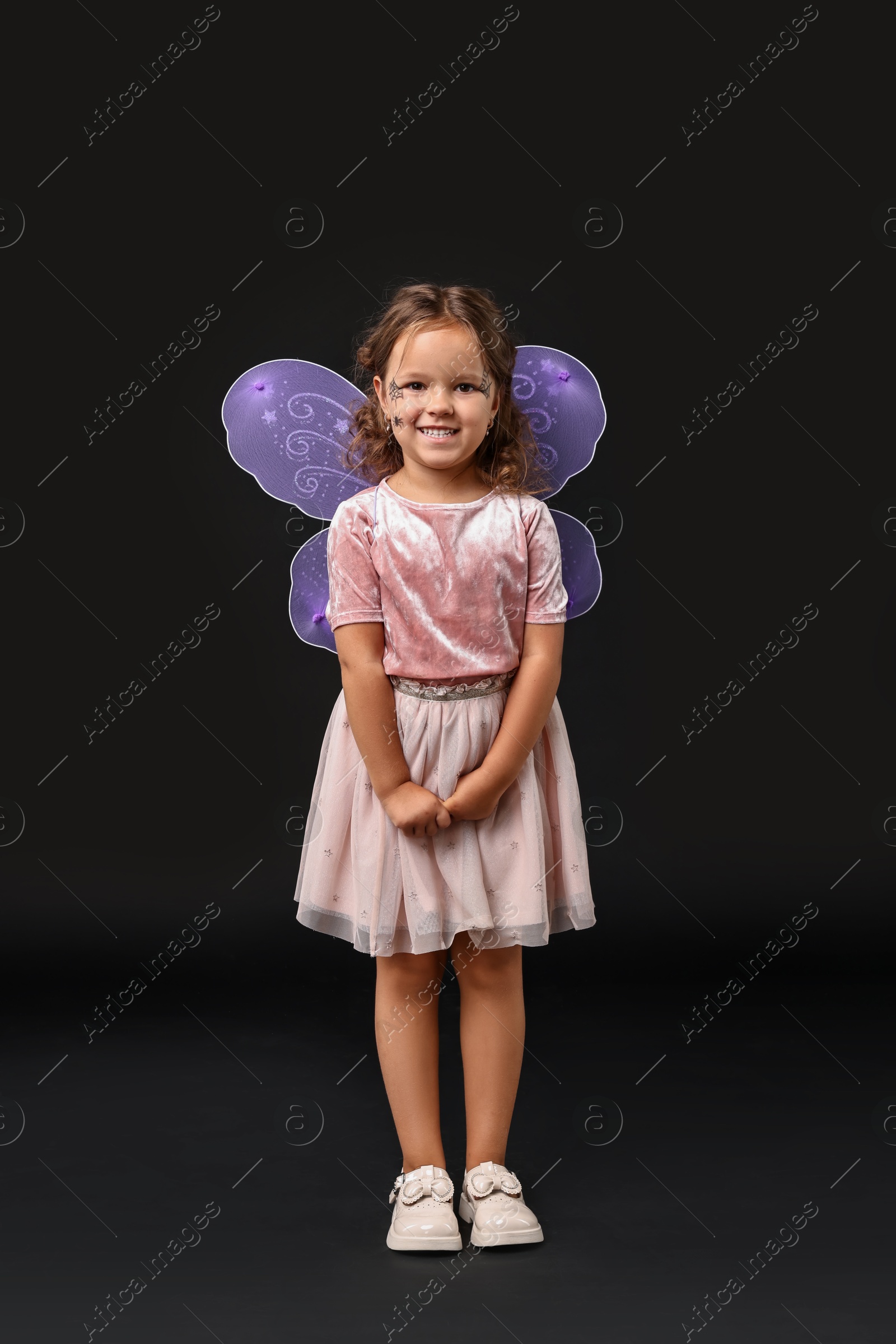 Photo of Cute girl dressed like fairy on black background. Halloween costume