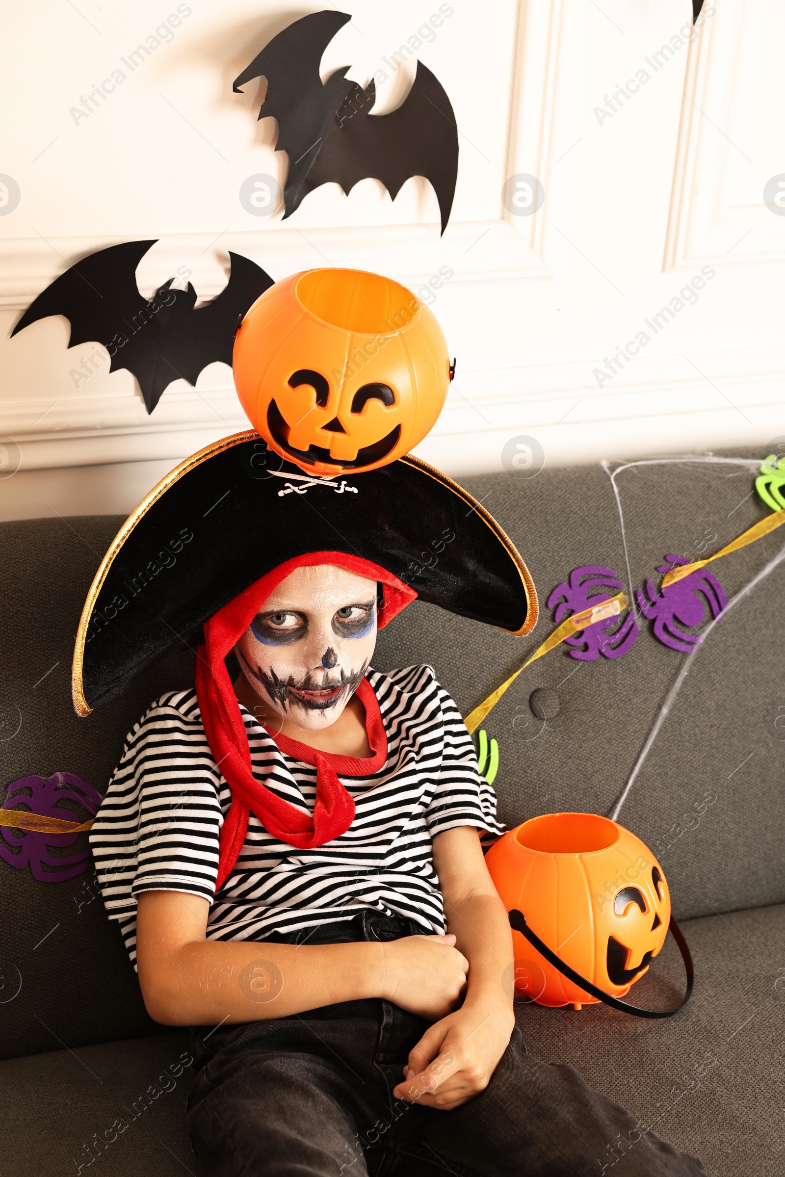 Photo of Funny boy with Halloween decor dressed like pirate on sofa indoors