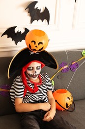 Photo of Funny boy with Halloween decor dressed like pirate on sofa indoors