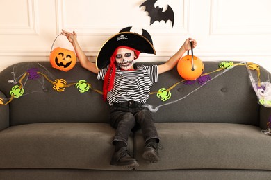 Photo of Funny boy with Halloween decor dressed like pirate on sofa indoors