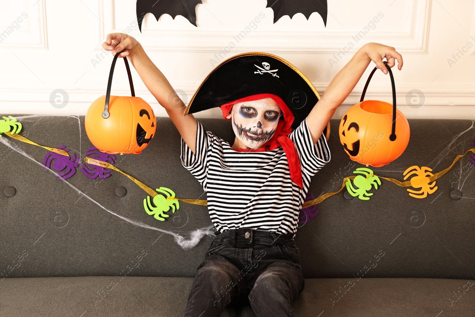 Photo of Funny boy with different Halloween decor dressed like pirate on sofa indoors