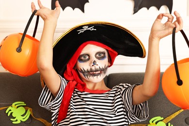 Photo of Funny boy with different Halloween decor dressed like pirate on sofa indoors