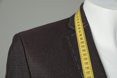 Photo of Semi-ready jacket with tailor's measuring tape on mannequin against grey background, closeup