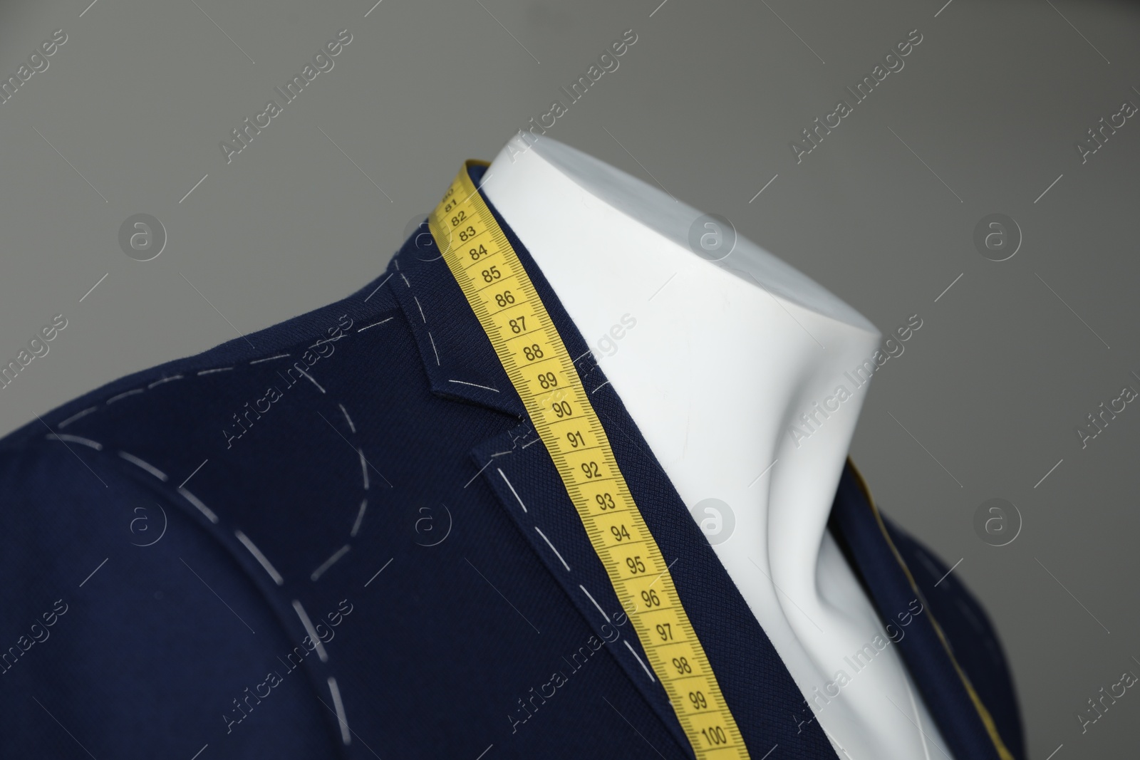 Photo of Semi-ready jacket with tailor's measuring tape on mannequin against grey background, closeup