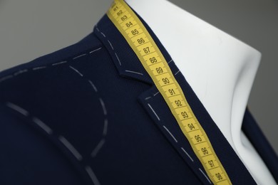 Semi-ready jacket with tailor's measuring tape on mannequin against grey background, closeup