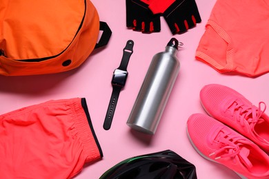 Bicycle helmet, sportswear, sneakers, thermo bottle and wristwatch on pink background, flat lay