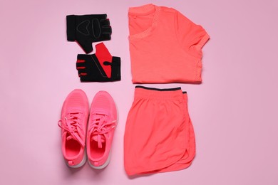 Sportswear, sneakers and fingerless cycling gloves on pink background, flat lay