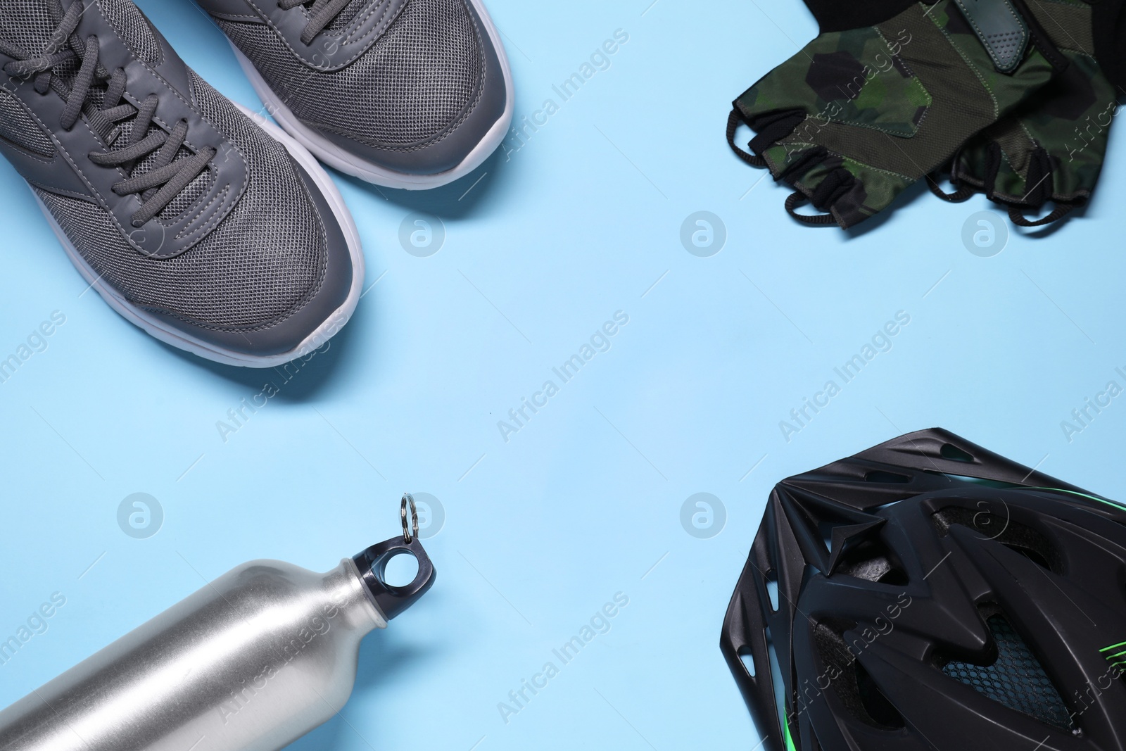 Photo of Bicycle helmet, sneakers, thermo bottle and fingerless cycling gloves on light blue background, flat lay. Space for text