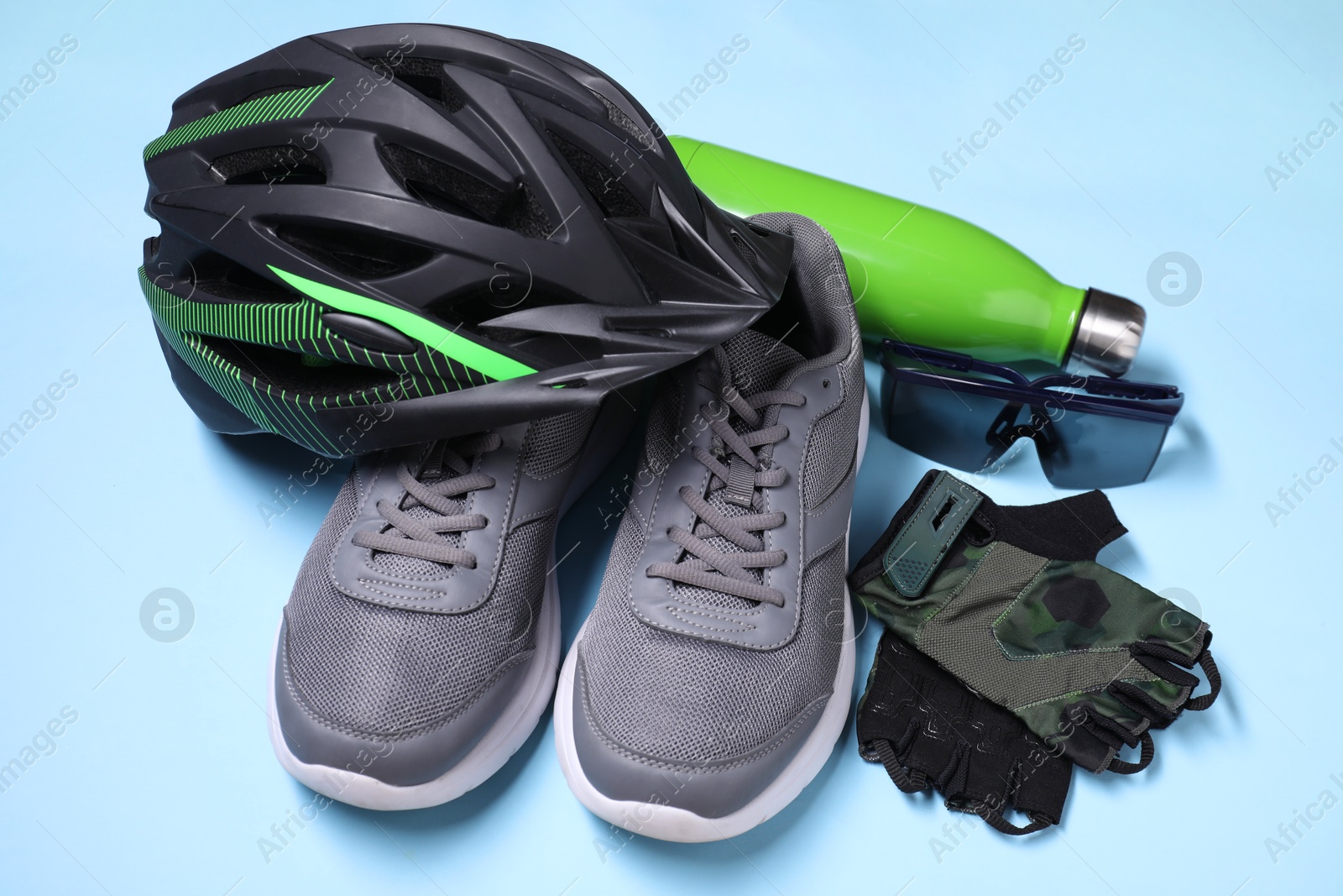 Photo of Bicycle helmet, sneakers, thermo bottle, fingerless gloves and goggles on light blue background