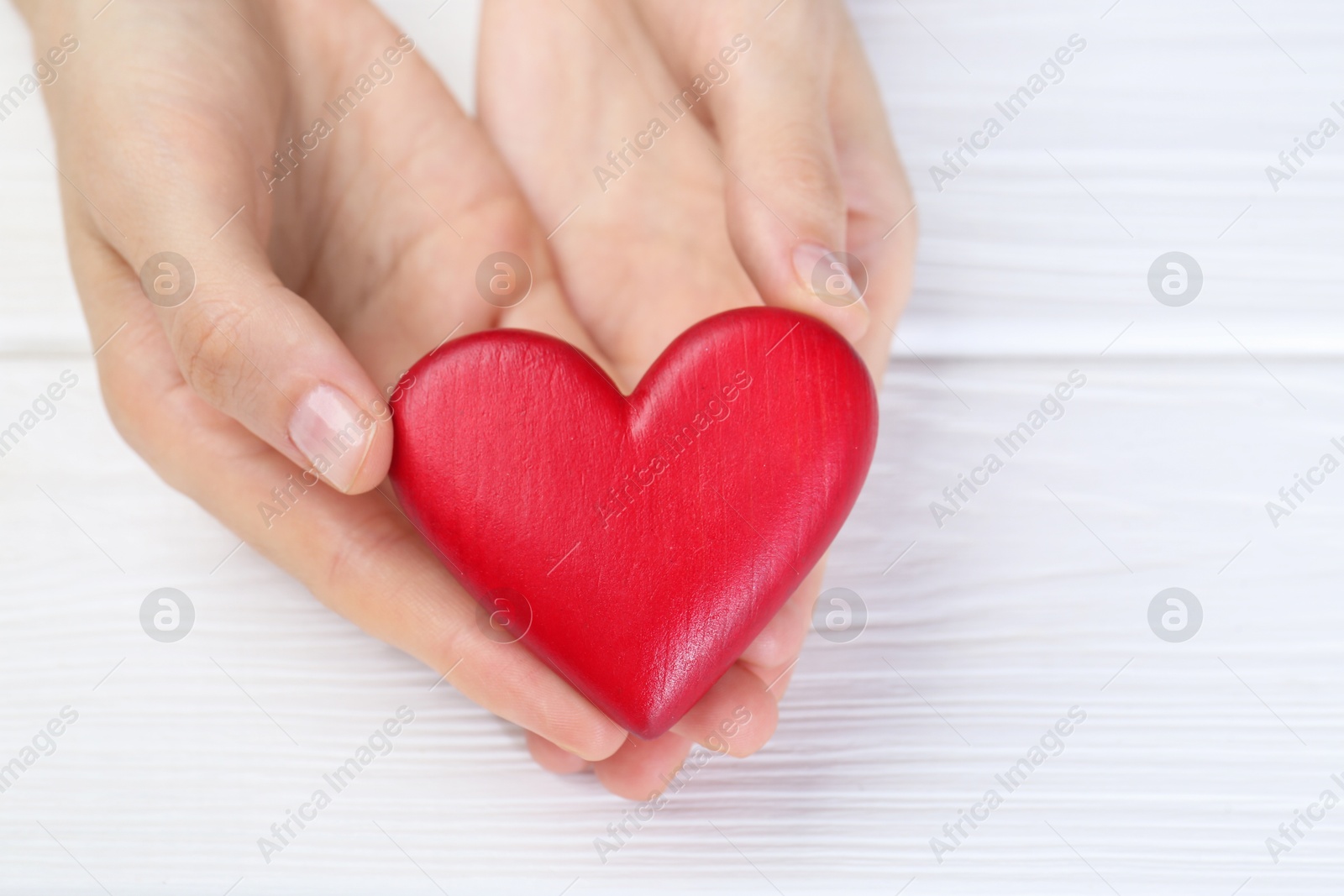 Photo of Woman holding red heart at white wooden table, closeup