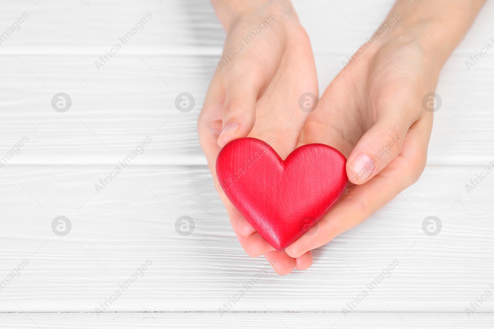 Photo of Woman holding red heart at white wooden table, closeup. Space for text