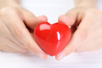 Photo of Woman holding red heart at white wooden table, closeup