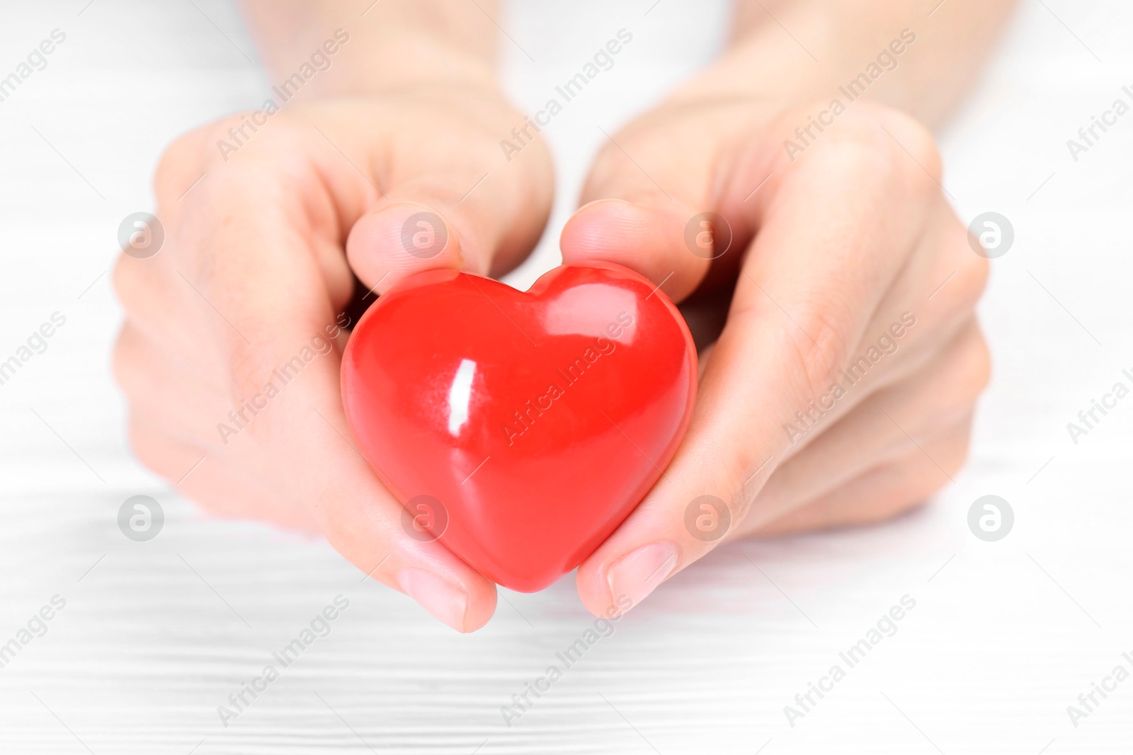 Photo of Woman holding red heart at white wooden table, closeup