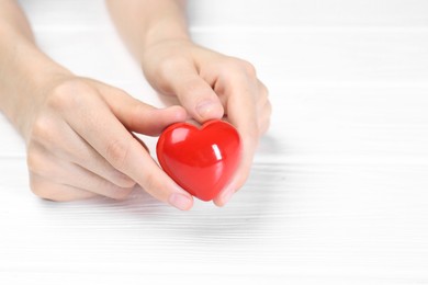 Photo of Woman holding red heart at white wooden table, closeup. Space for text