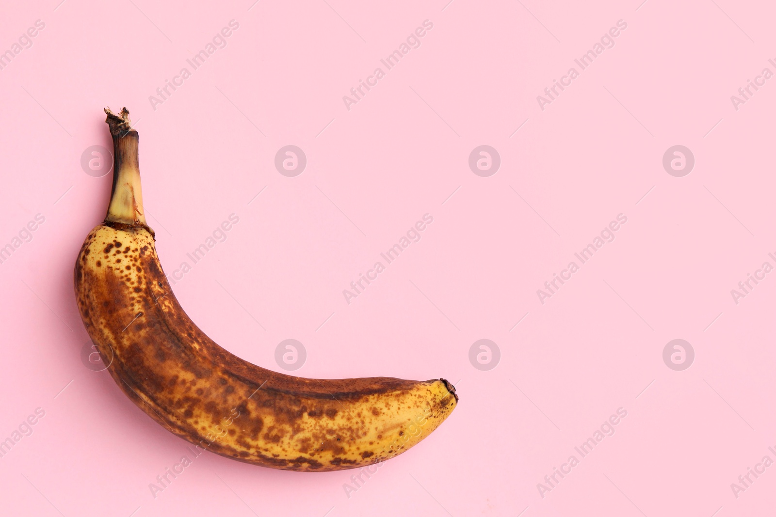 Photo of Overripe banana with dark spots on pink background, top view. Space for text