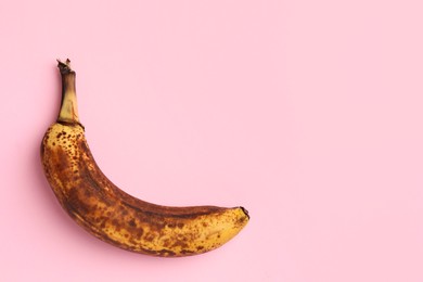 Photo of Overripe banana with dark spots on pink background, top view. Space for text