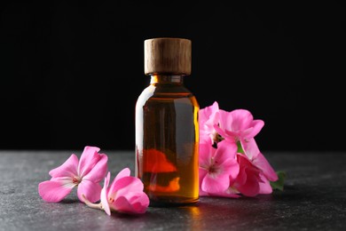 Photo of Bottle of geranium essential oil and beautiful flowers on black table, closeup