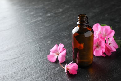 Photo of Bottle of geranium essential oil and beautiful flowers on black table, closeup. Space for text