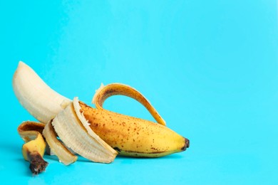 Photo of Ripe banana with dark spots on light blue background. Space for text