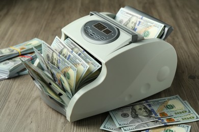 Photo of Money counter machine with dollar banknotes on wooden table