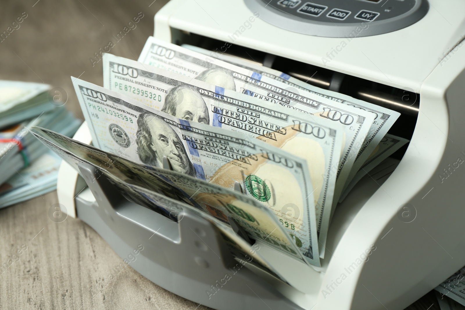 Photo of Money counter machine with dollar banknotes on wooden table, closeup