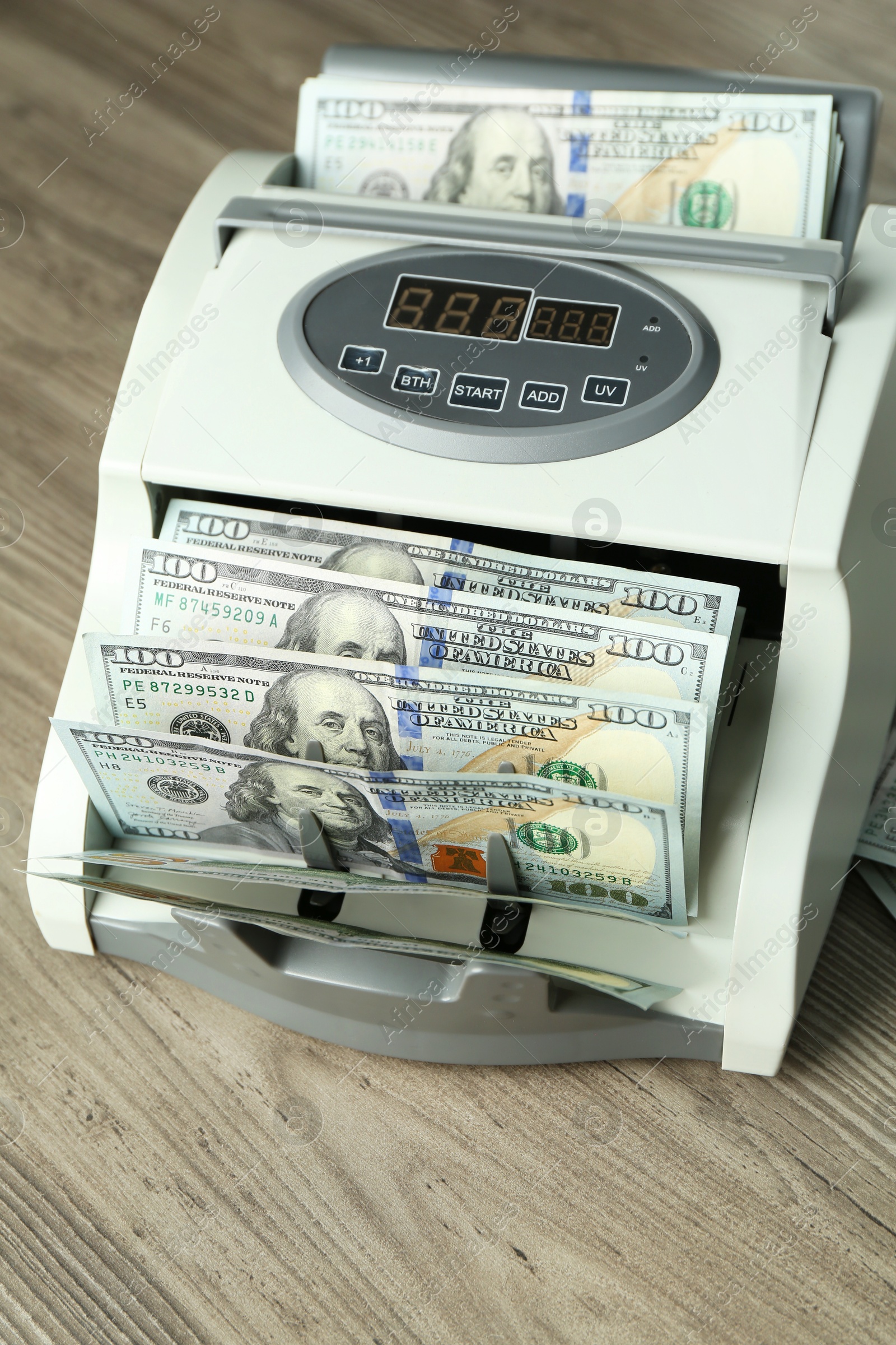 Photo of Money counter machine with dollar banknotes on wooden table