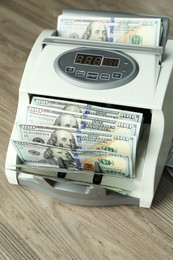 Photo of Money counter machine with dollar banknotes on wooden table