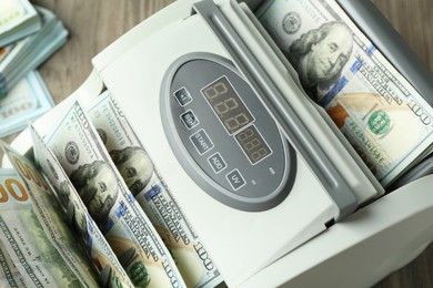 Photo of Money counter machine with dollar banknotes on table, closeup