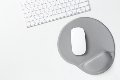 Photo of Keyboard, mouse and mousepad with arm rest on white table, top view. Space for text