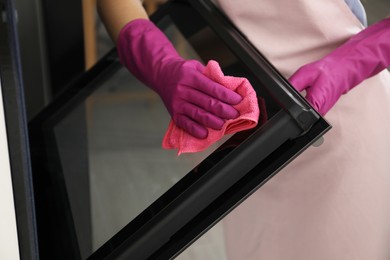 Photo of Woman wiping electric oven with rag in kitchen, closeup