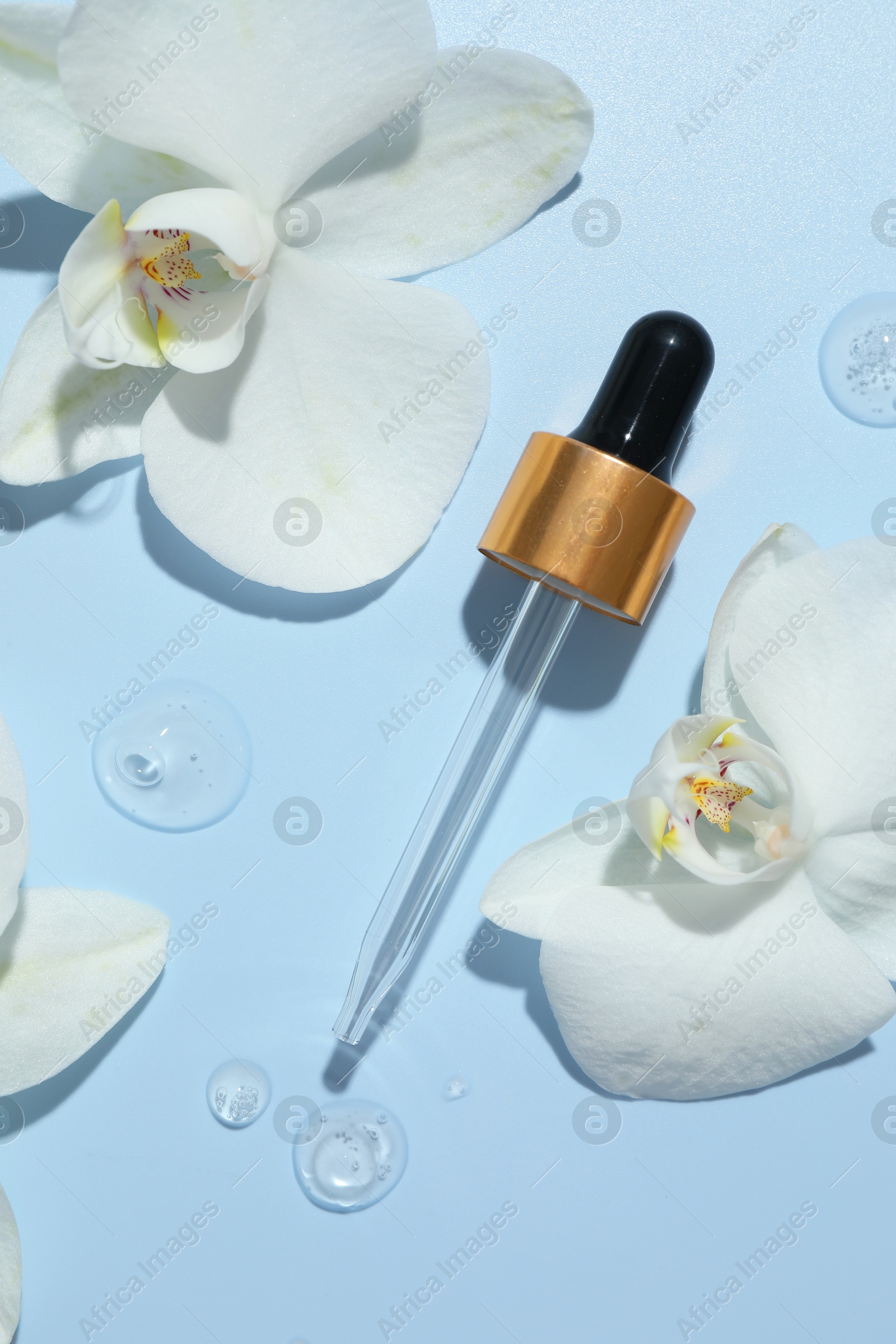 Photo of Beautiful orchid flowers and dropper with cosmetic product in water on light blue background, flat lay