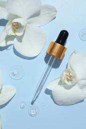 Photo of Beautiful orchid flowers and dropper with cosmetic product in water on light blue background, flat lay