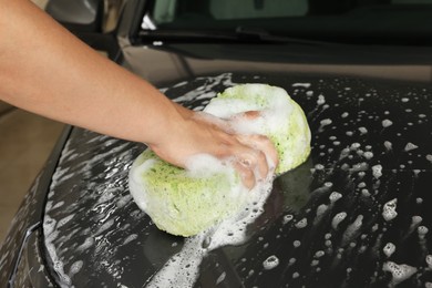 Man washing car hood with sponge indoors, closeup