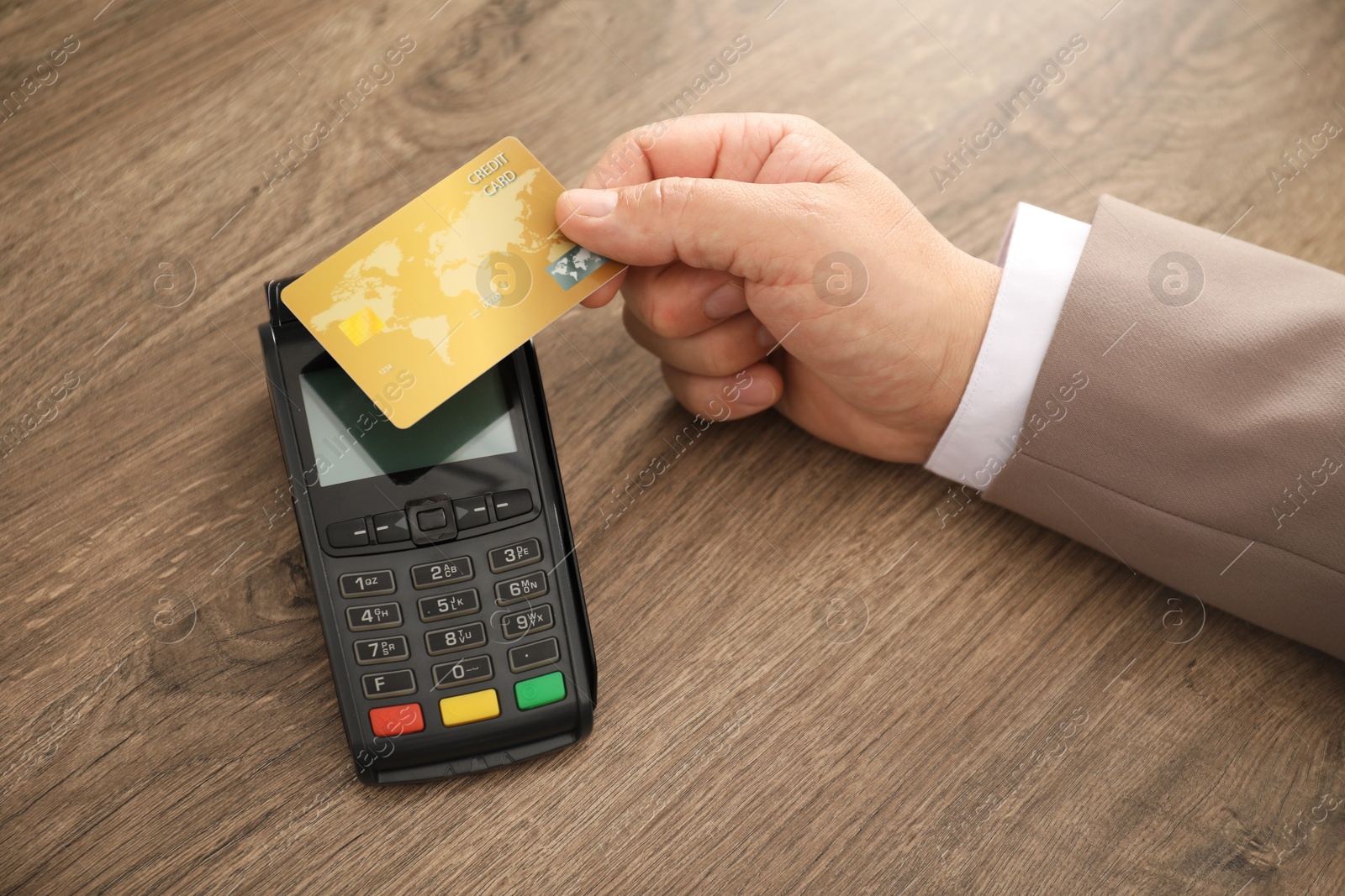 Photo of Man with credit card using terminal at wooden table, closeup