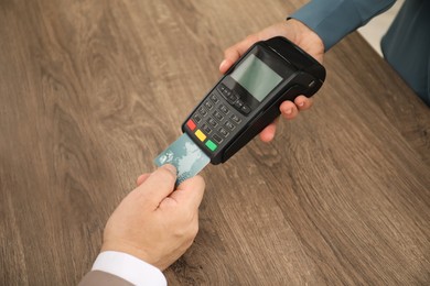 Woman taking payment from client via credit card terminal at wooden table, closeup