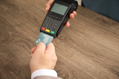 Photo of Woman taking payment from client via credit card terminal at wooden table, closeup