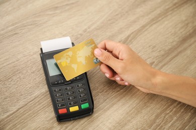 Photo of Woman with credit card using terminal at wooden table, closeup