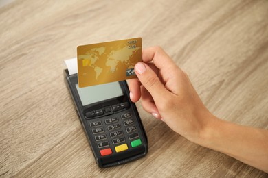 Photo of Woman with credit card using terminal at wooden table, closeup