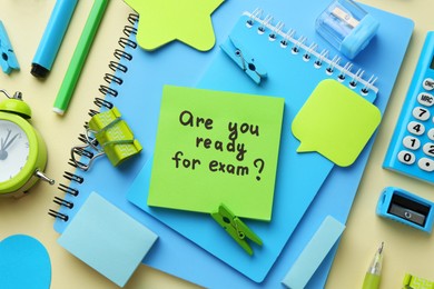 Paper note with question Are You Ready For Exam and stationery on pale yellow background, flat lay