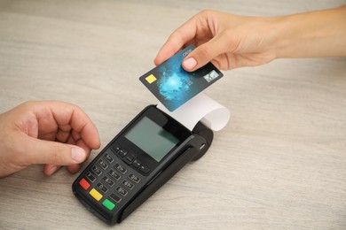 Man taking payment from client via credit card terminal at wooden table, closeup